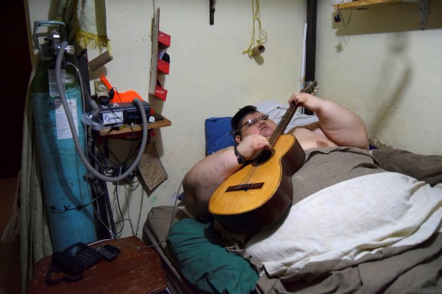 Juan Pedro, 32, plays a guitar as he waits for paramedics to transport him to a hospital in Guadalajara, to undergo treatment in order to shed excess from his 500-kilo weight, in Aguascalientes, Mexico, November 15, 2016. Picture taken November 15, 2016. REUTERS/Liberto Urena FOR EDITORIAL USE ONLY. NO RESALES. NO ARCHIVES.