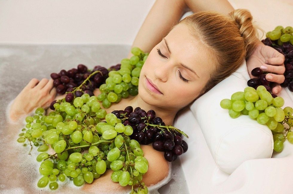 00550287 Young woman in bath with grapes