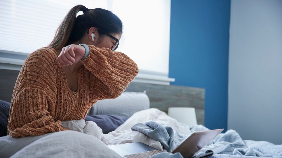 1 Woman coughing into elbow while sitting in bed