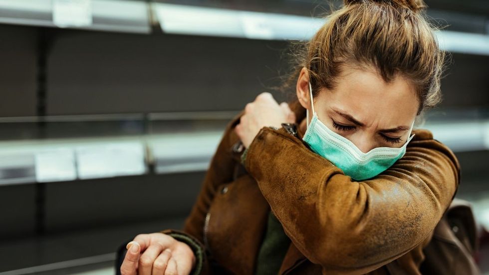 1 Woman with face mask sneezing into elbow while shopping in grocery store