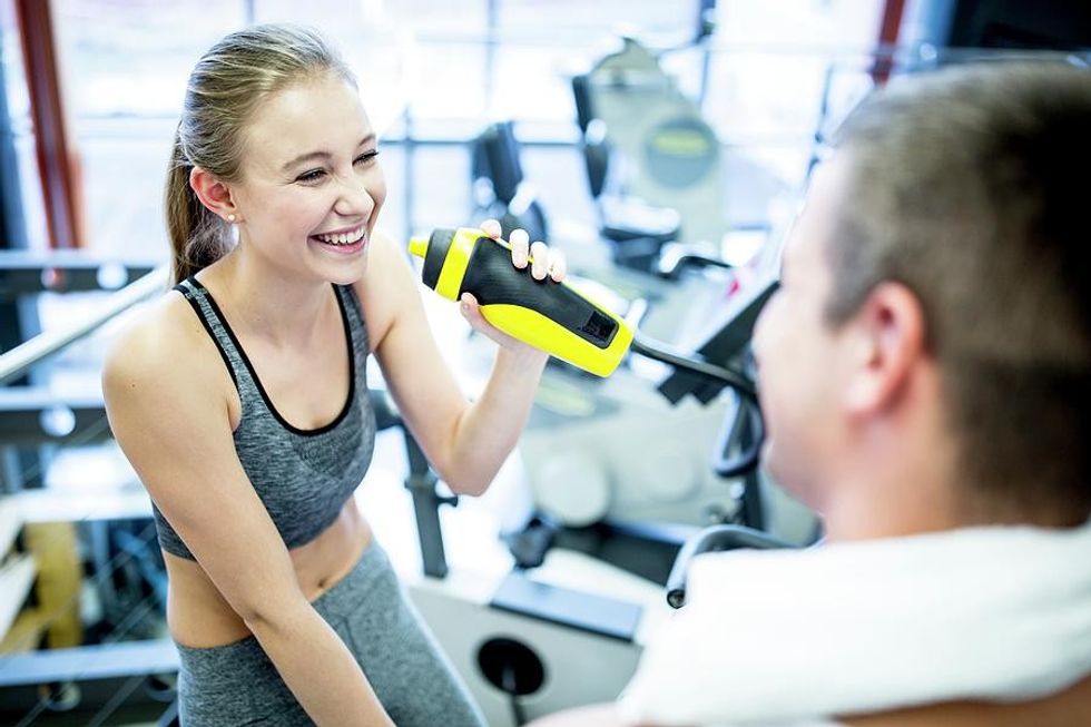 111359480 young sporty couple drinking water after training in gym