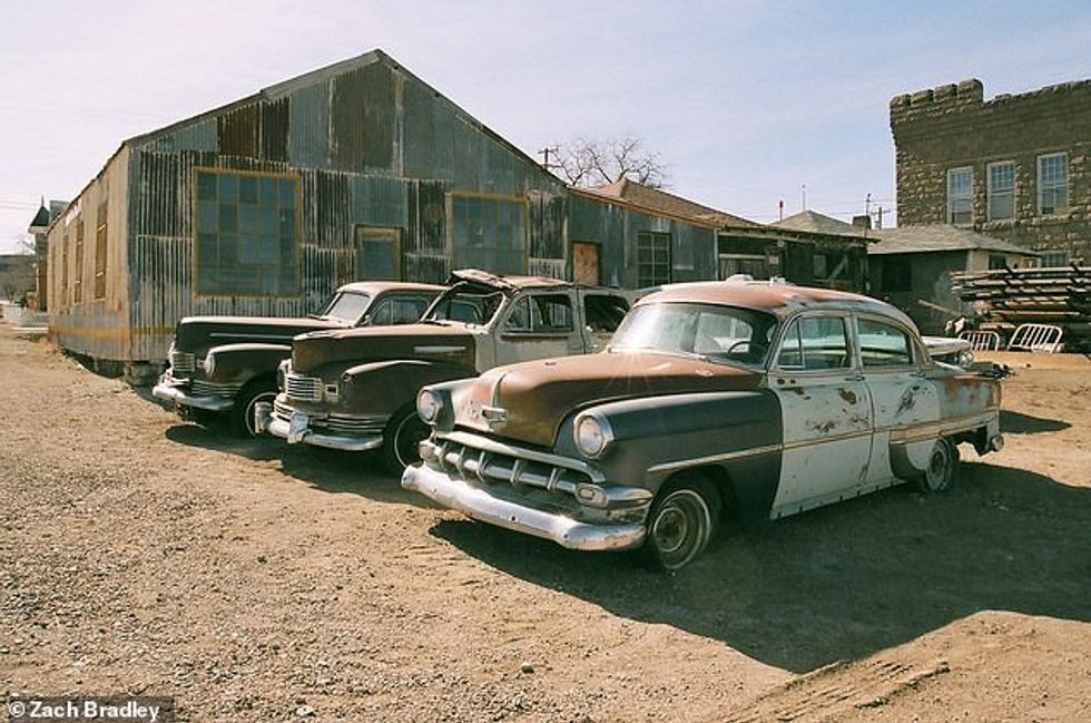 25626996 8083141 Old cars lie next to some dilapidated buildings in the town of G a 5 1583761942709
