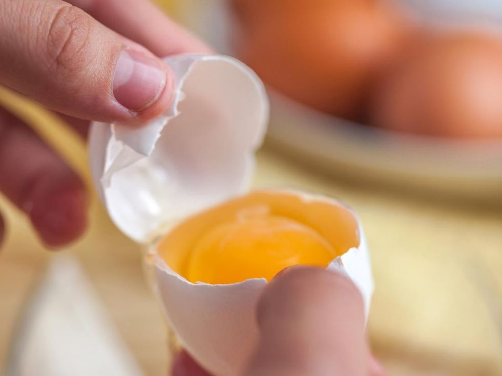 a hand holding a cracked egg showing a yolk