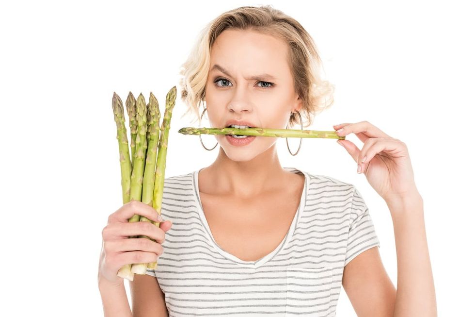 A Woman Holding Up Asparagus and Biting It