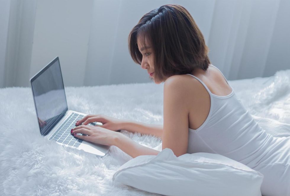 asian woman working on a laptop on bed free photo
