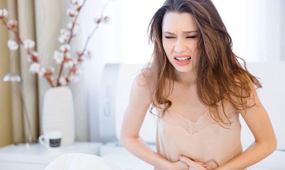 Beautiful young woman in lingerie sitting on bed and suffering from abdominal pain