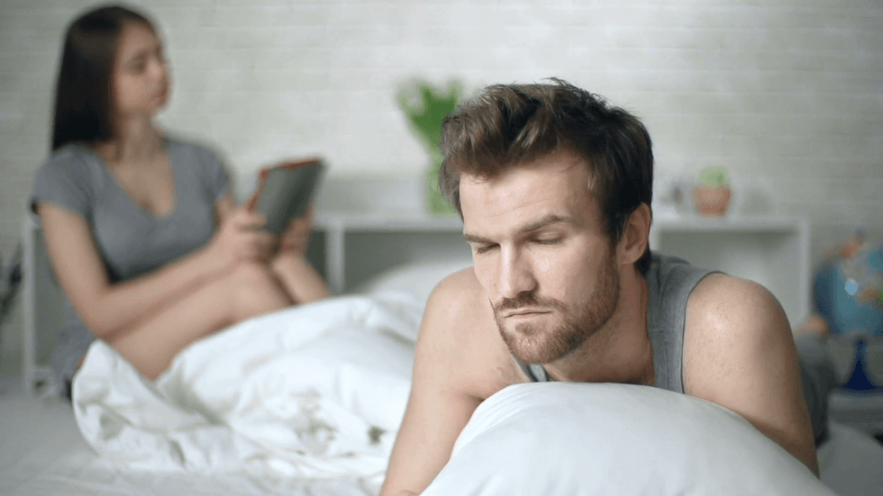 close up of man unhappy with his relationship with woman sitting in bed in with touchpad in the background v1qgg vd t