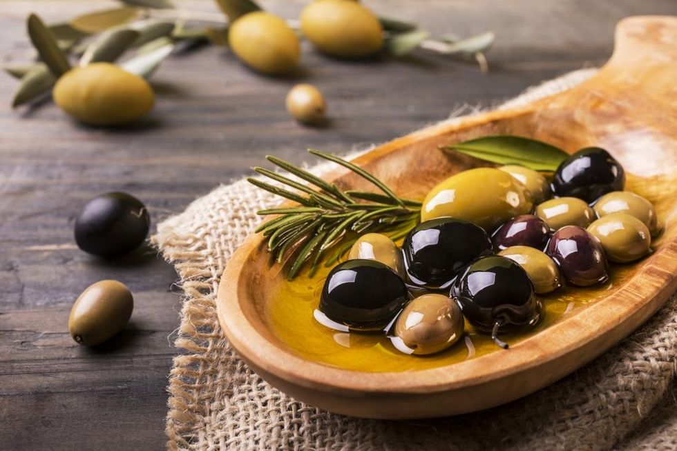 different types of olives in oil in wooden bowl