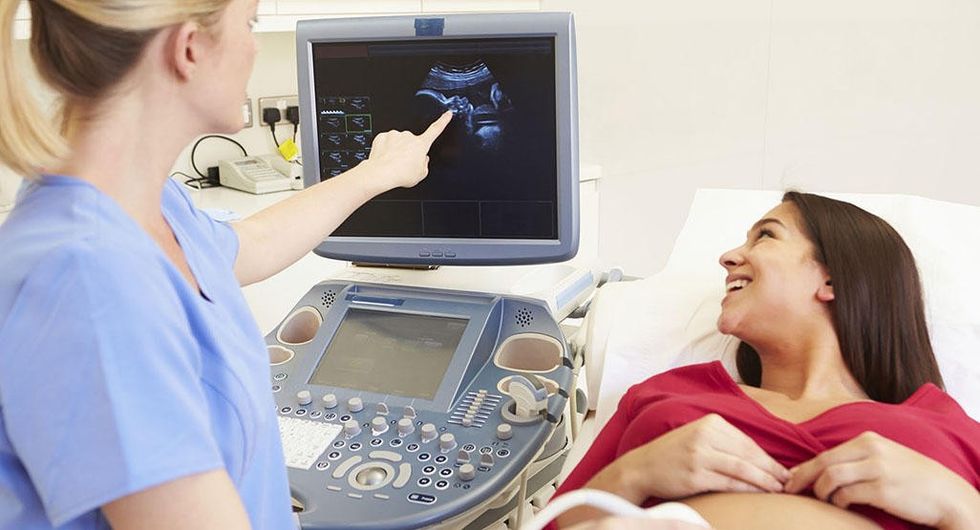 female nurse performing ultrasound on pregnant woman in exa