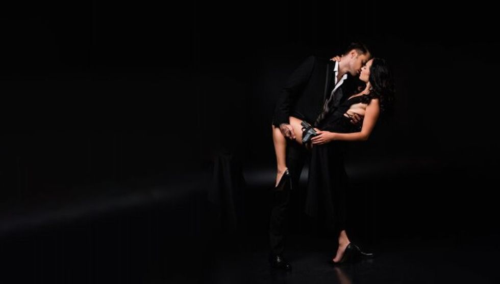 full length of man lifting leg of dangerous and armed woman in dress and kissing her on black 400 239348554