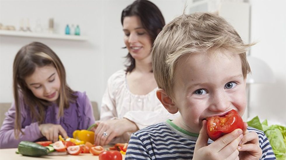 Germany, Bavaria, Munich, Mother and daughter preparing salad, son eating