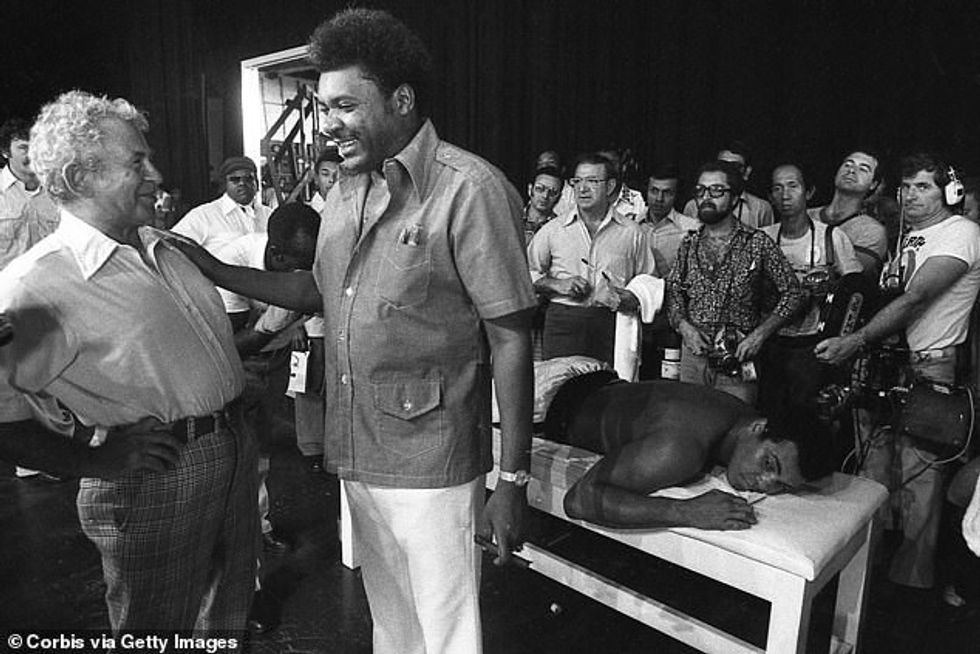 Great American writer Norman Mailer (left) chats with Rumble promoter Don King a year later, as Muhammad Ali lays behind them on a massage table