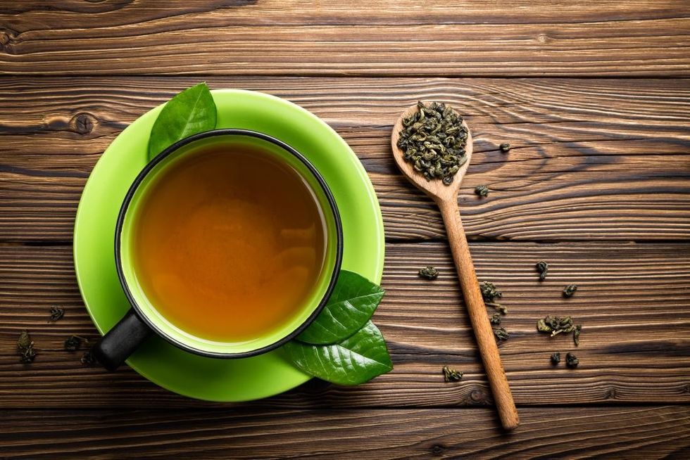 green tea in cup with tea leaves on wooden spoon
