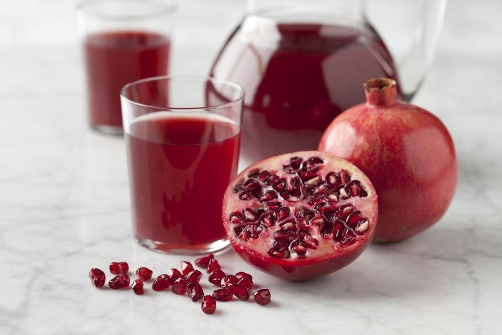 halves pomegranate with seeds and pomegranate juice on marbled surface