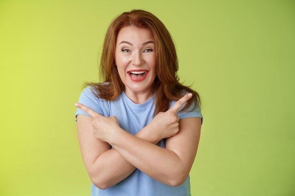 happy carefree entushiastic redhead funny mature female having fun positive attitude cross arms body pointing sideways show left right products laughing happily like both choices green wall 1258 46301