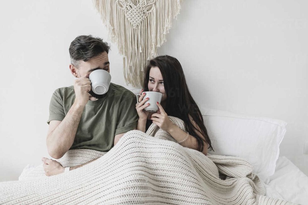 happy couple sitting in bed drinking coffee having fun KMKF00589