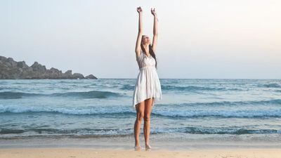 2018/08/a-young-brunette-woman-standing-on-the-beach-with-her-hands-up.jpg