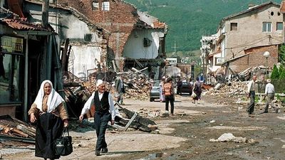 2018/09/people-walk-the-street-past-the-destruction-in-peja-kosovo-br4hey.jpg