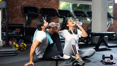 2022/11/indian-young-couple-gym-resting-taking-break-from-exercise-drinking-wate.jpg