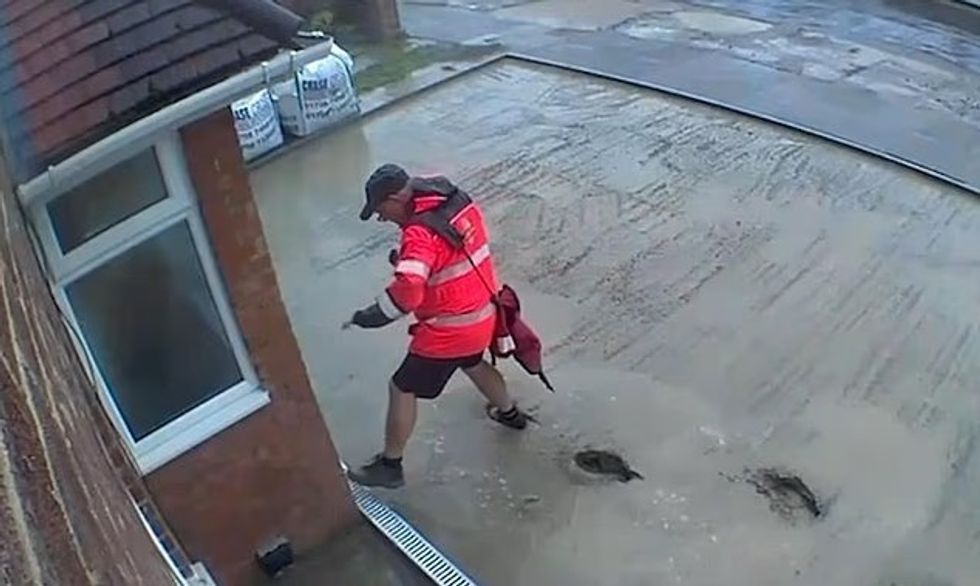 I pavetëdijshëm, postieri britanik ecë nëpër çimenton e lagësht të saposhtruar në oborrin e një shtëpie