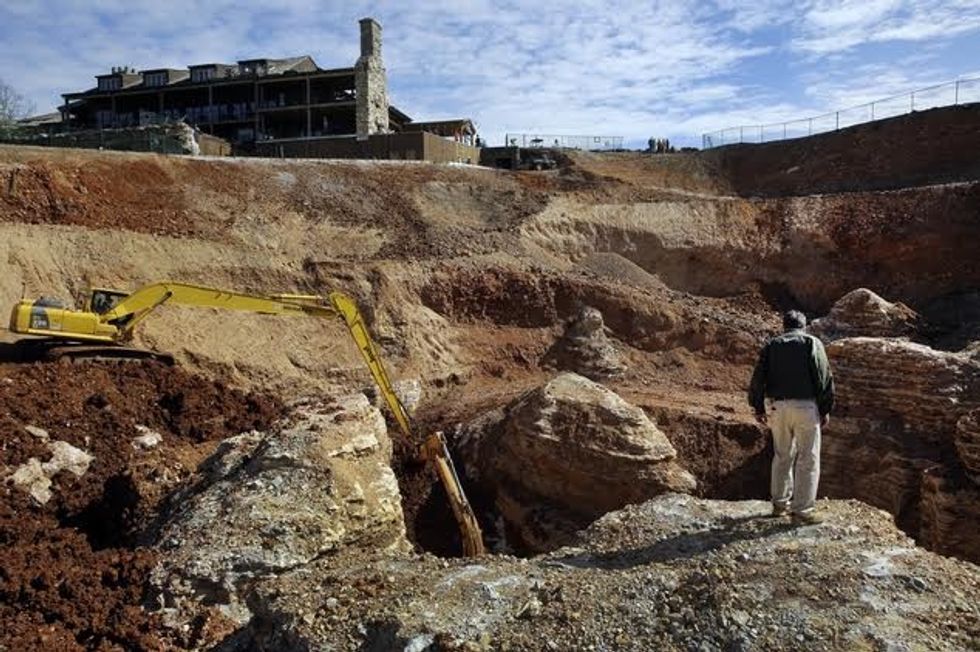 In this photo made Thursday, April 14, 2016, Johnny Morris, founder of Bass Pro Shops, looks over the edge of a massive sinkhole at his Top of the Rock Golf Course in Ridgedale, Mo. After days of heavy rain, the sinkhole appeared along the putting green and very close to a structure housing the the clubhouse, restaurants and a pro shop shown at top left. (AP Photo/Jeff Roberson)