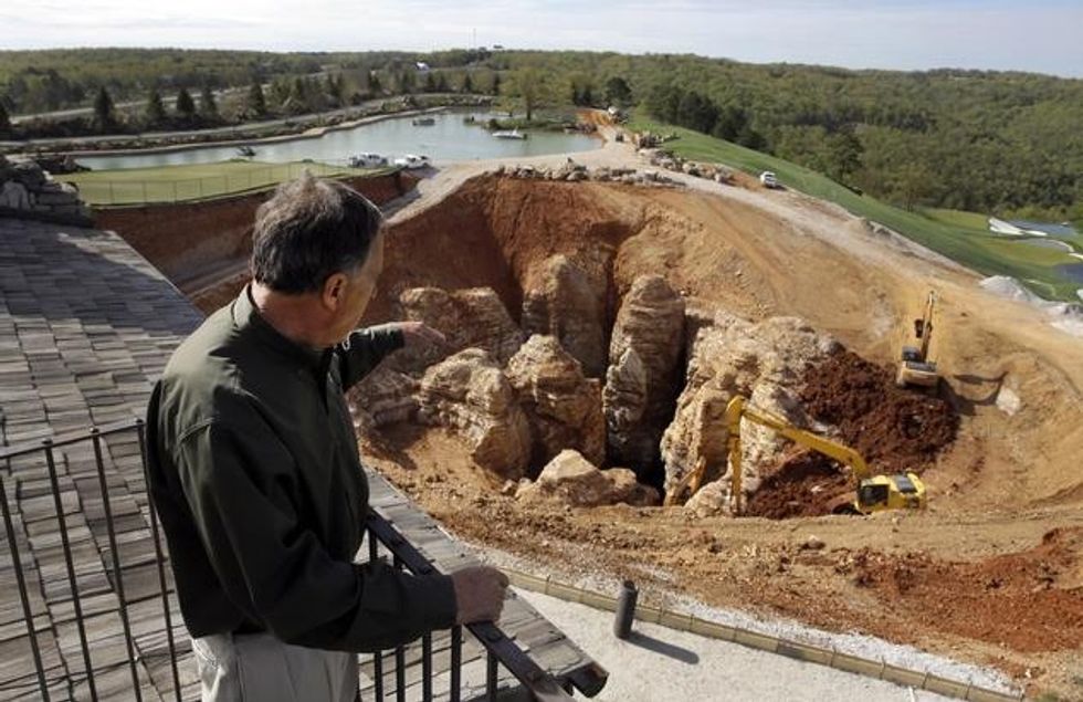 In this photo made Thursday, April 14, 2016, Johnny Morris, founder of Bass Pro Shops, points to a massive sinkhole that opened up on his golf course during heavy rain last spring in Ridgedale, Mo. Experts urged Morris to fill the hole with clay and boulders, but he was intrigued by the possibility that an unknown cave system was at the root of the sinkhole which he believes could tie into other caves nearby including one he himself discovered over two decades ago. (AP Photo/Jeff Roberson)