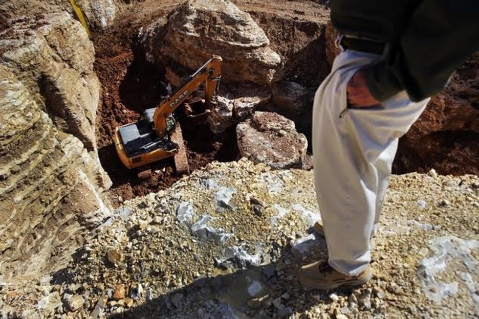 In this photo made Thursday, April 14, 2016, Johnny Morris, founder of Bass Pro Shops, stands on the edge of a huge sinkhole as a backhoe works below in Ridgedale, Mo. At the bottom of a hole, a backhoe painstakingly moves dirt to a ledge, where a second backhoe reaches down and removes it, a scoop at a time, in an effort to unearth a possible hidden cave system. (AP Photo/Jeff Roberson)