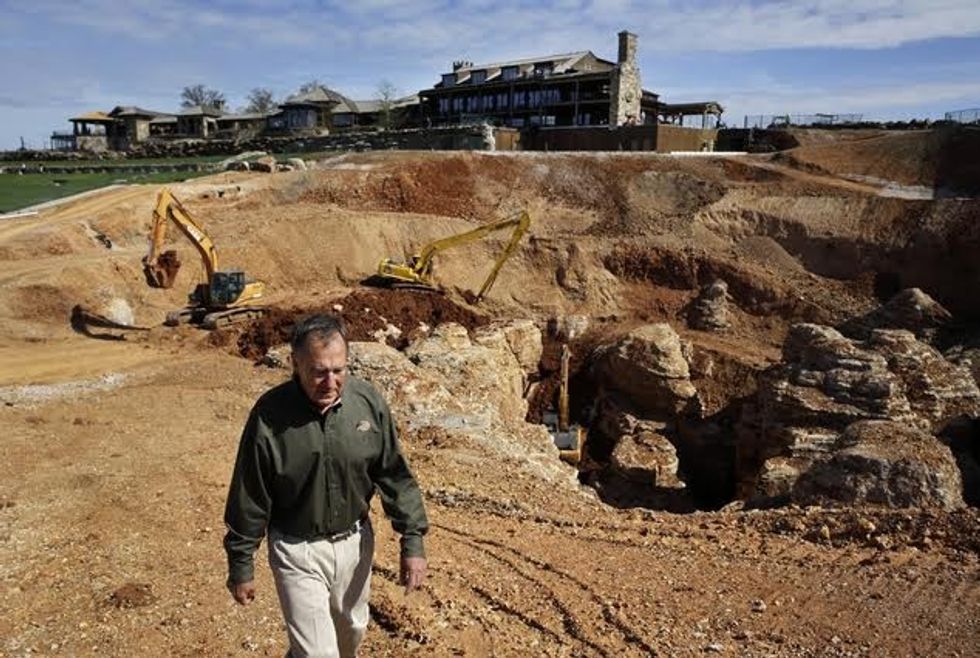 In this photo made Thursday, April 14, 2016, Johnny Morris, founder of Bass Pro Shops, walks around the edge of a massive sinkhole that opened up last spring on his golf course in Ridgedale, Mo. Morris, a cave enthusiast for years, believes the sinkhole and a cave he discovered about a half-mile away in 1993 are connected after water from a pond on the golf course drained into the hole and began pouring out the entrance to the cave. (AP Photo/Jeff Roberson)