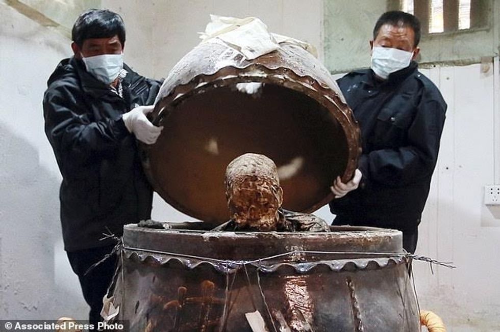In this photo taken Sunday Jan. 10, 2016, men remove the top of a jar containing the mummified body of revered Buddhist monk Fu Hou in Quanzhou city in southeastern China's Fujian province. The monk, who died in 2012 at the age of 94, was prepared for mummification by his temple to commemorate his devotion to Buddhism. The mummifed remains were then treated and covered in gold leaf, a practice reserved for holy men in some areas with strong Buddhist traditions. (Chinatopix via AP) CHINA OUT