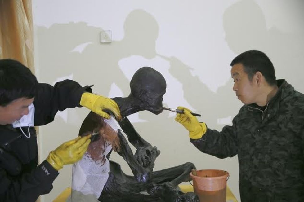 In this photo taken Thursday Jan. 14, 2016, men apply lacquer on the mummified body of revered Buddhist monk Fu Hou in Quanzhou city in southeastern China's Fujian province. The monk, who died in 2012 at the age of 94, was prepared for mummification by his temple to commemorate his devotion to Buddhism. The mummifed remains were then treated and covered in gold leaf, a practice reserved for holy men in some areas with strong Buddhist traditions. (Chinatopix via AP) CHINA OUT