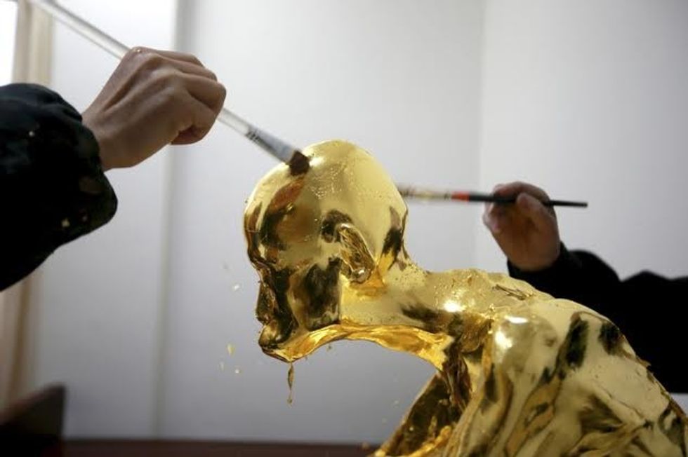In this photo taken Wednesday March 16, 2016, men apply gold leaf on the mummified body of revered Buddhist monk Fu Hou in Quanzhou city in southeastern China's Fujian province. The monk, who died in 2012 at the age of 94, was prepared for mummification by his temple to commemorate his devotion to Buddhism. The mummifed remains were then treated and covered in gold leaf, a practice reserved for holy men in some areas with strong Buddhist traditions. (Chinatopix via AP) CHINA OUT