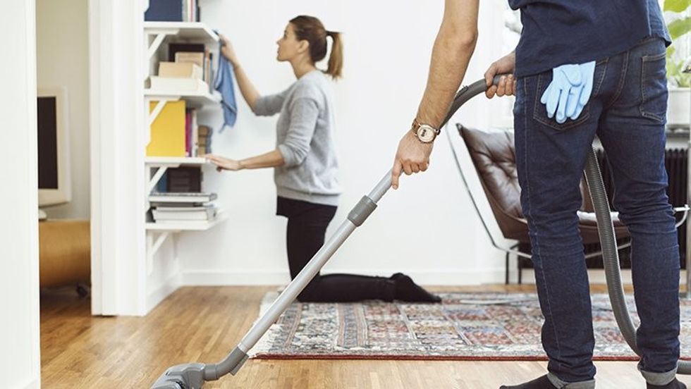 low section of man vacuuming floor while woman cleaning shelves in background at home 562452153 599b4fb2c412440013253d30