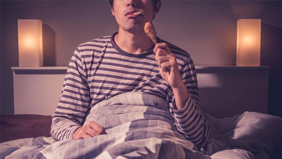 man in bed eating chicken leg