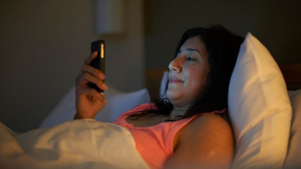 mature woman in bed looking at her phone GettyImages 638685121