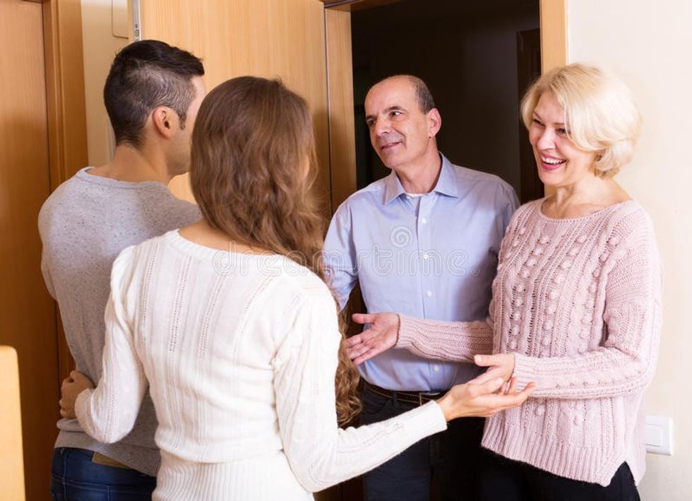 meeting door happy young couple inviting elderly parents to come inside 55049719