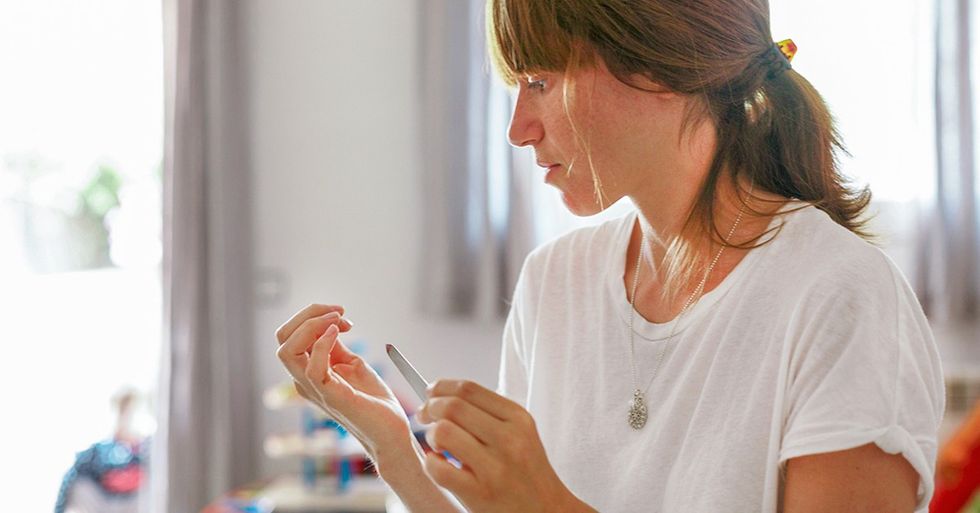 Mid adult woman at home using nail file facebook