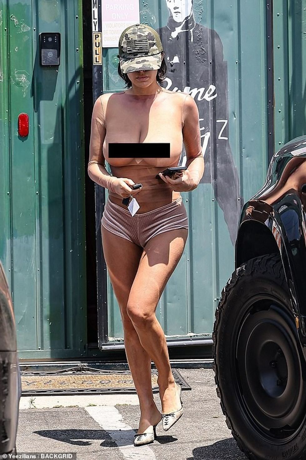 Një kapele me printe kamuflazhi mbroni flokët e saj të shkurtra brune, ndërsa ajo kthehej e sigurt në seancën e saj pas nxirjes në makinë