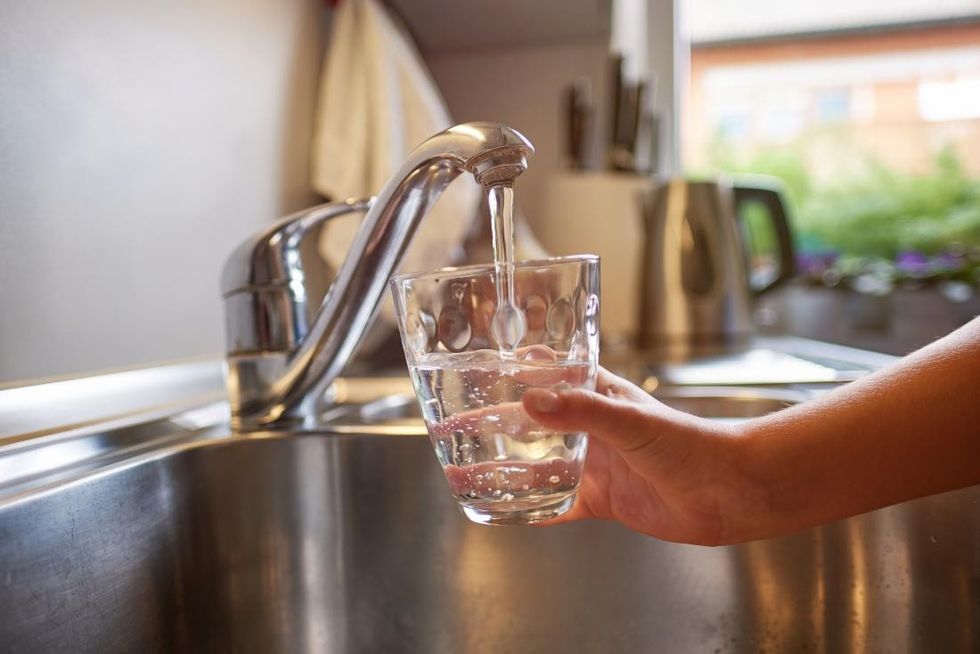 person pouring water from tap into glass of water for treating cloudy urine