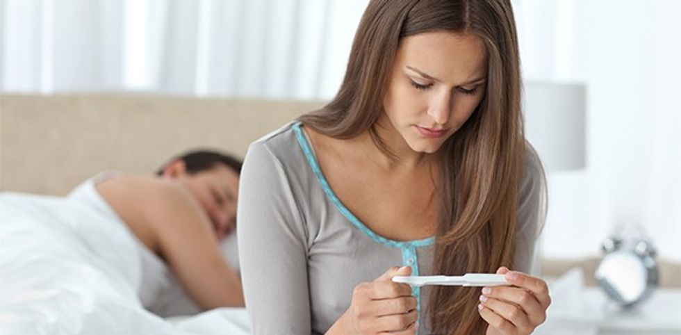 Pretty woman looking a pregnancy test while her boyfriend sleeping on the background ** Note: Shallow depth of field