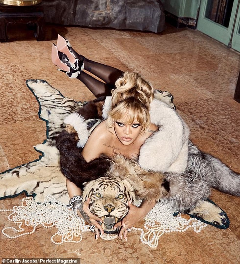 Rihanna dukej sensacionale në një foto tjetër ku u mbështjellë me një pallto të zezë ndërsa ishte shtrirë në një qilim të bardhë tigër.