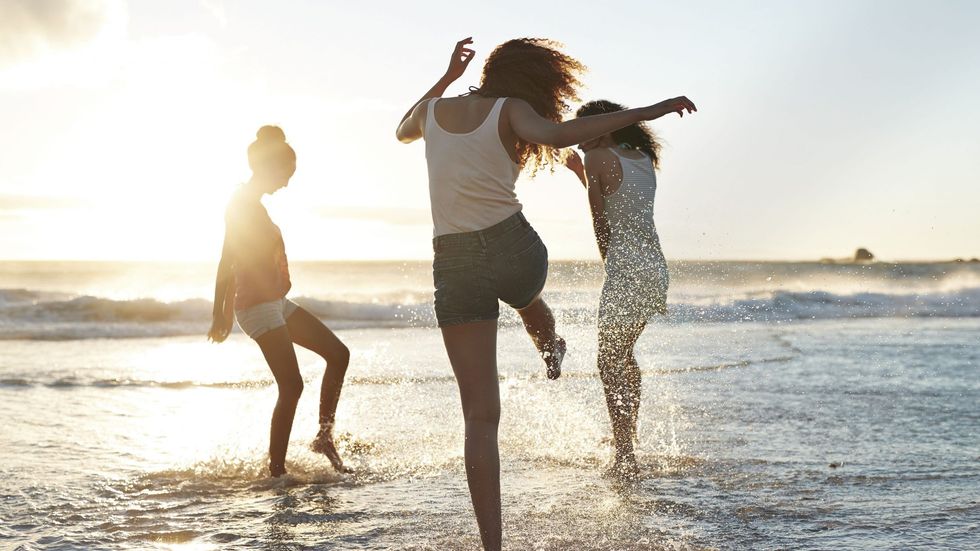 three young women kicking water and laughing on the beach 847741798 5a90af6e642dca0036d446fc scaled