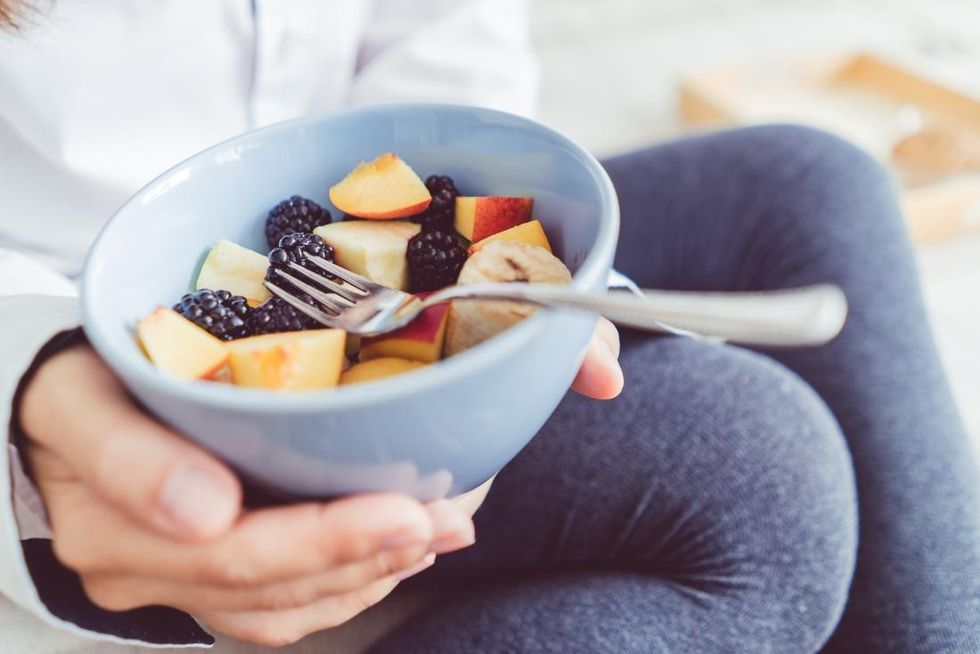 woman holding bowl of chopped up fresh fruit including apples and blackberries