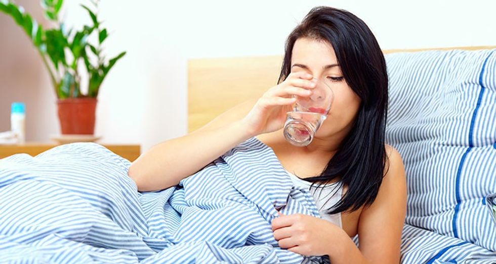 woman sick in bed drinking water