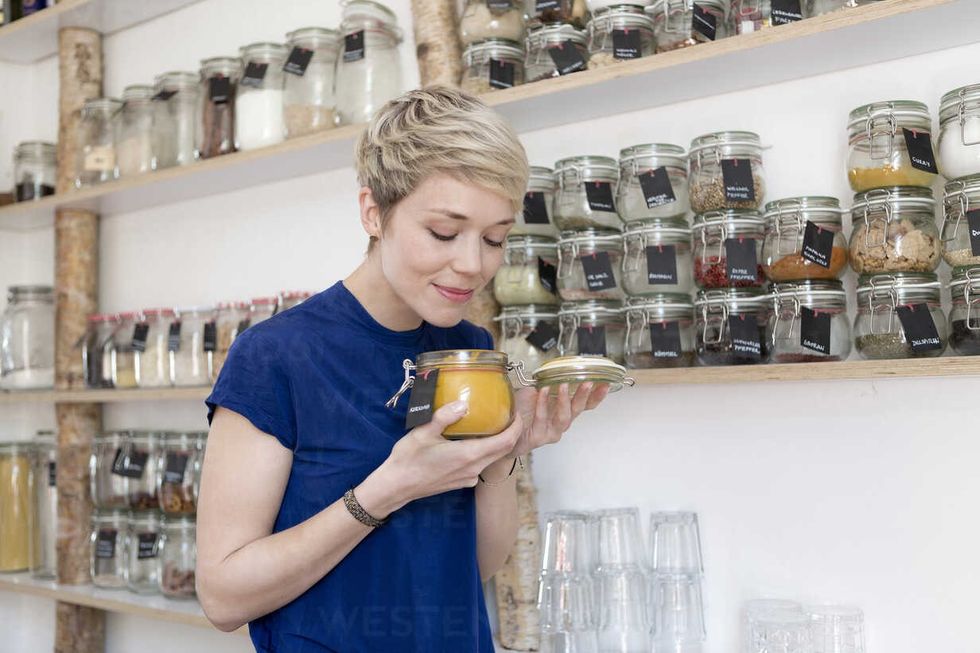 woman smelling at jar in front of spice shelf in kitchen FLLF00168