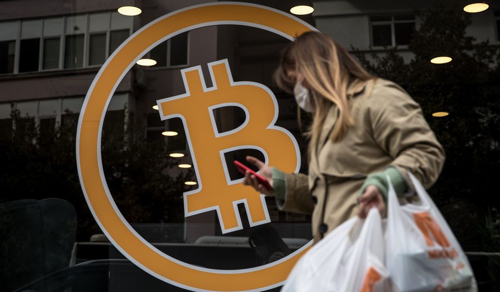 woman walks past bitcoin sign e1619252151144