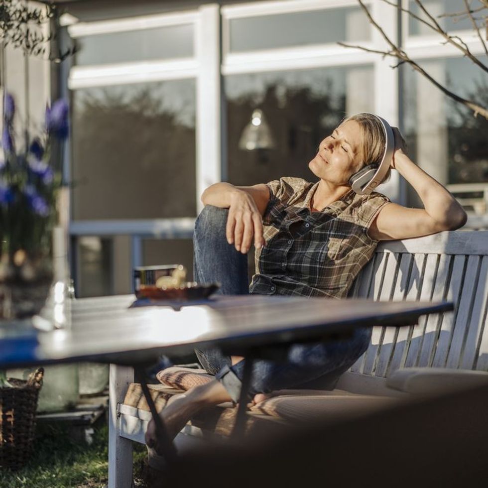 woman wearing headphones relaxing on garden bench royalty free image 1584981258