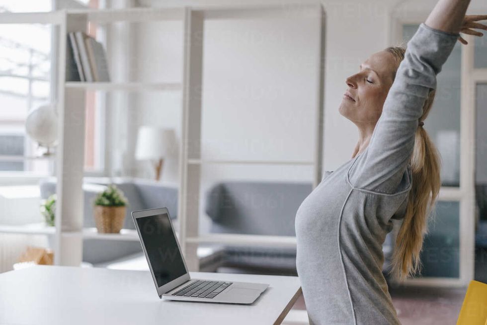 woman with laptop at desk in office stretching KNSF03576