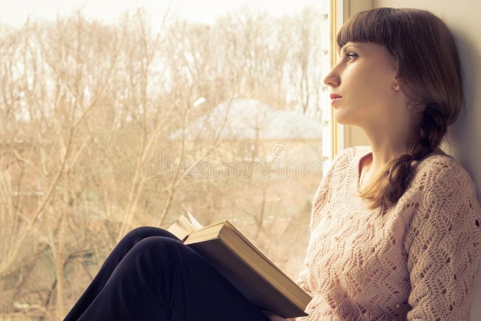 young adult girl reading book near window warm toned image 39389562