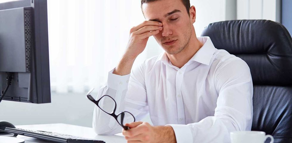 Young tired businessman rubbing his eye in the office