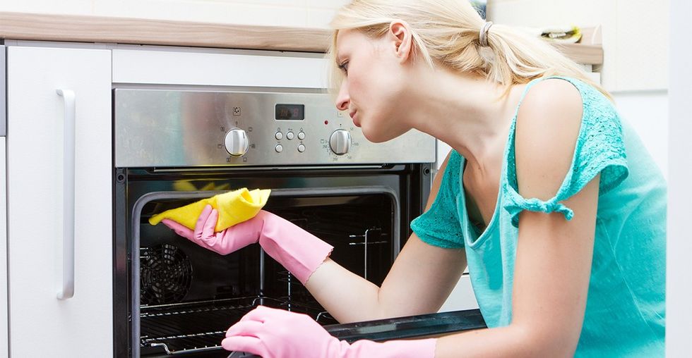 Young woman cleaning oven in the kitchen.